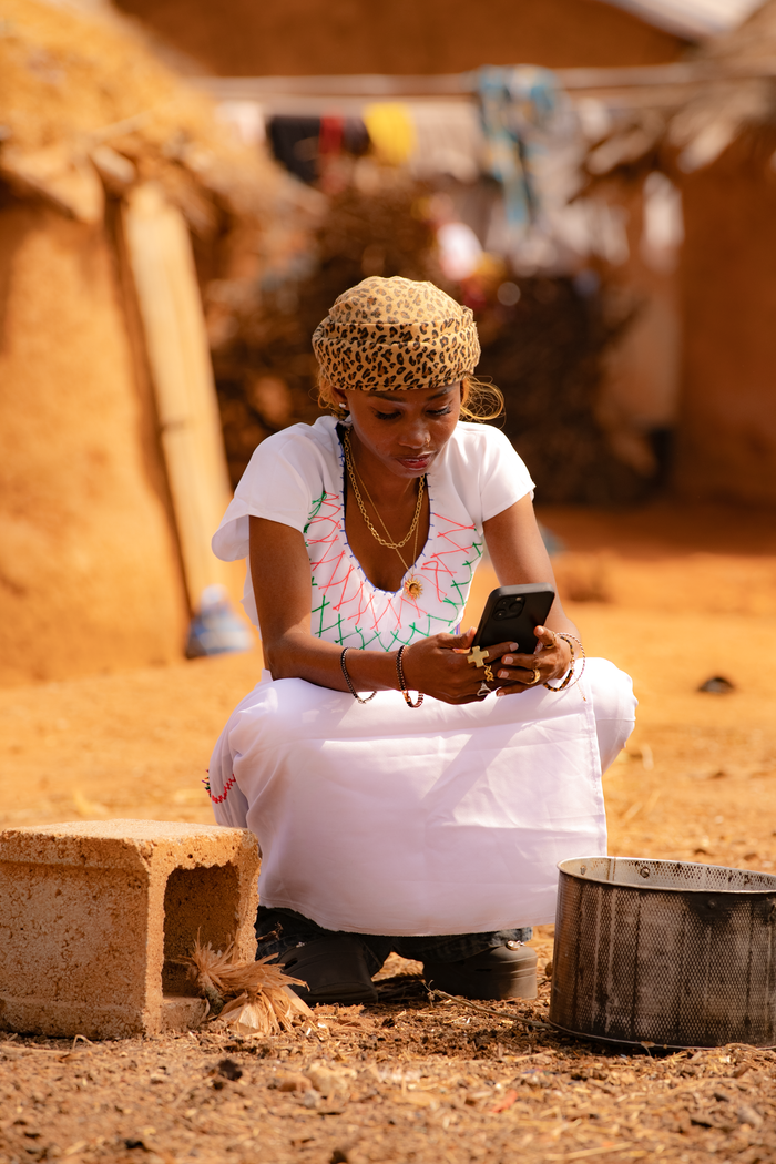 Young woman sitting outside, using a smartphone in a rural environment.