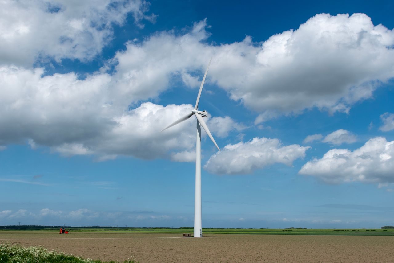 Lone wind turbine standing in a vast open field under a vibrant blue sky with fluffy clouds.
